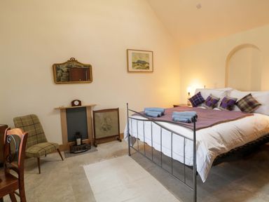 A bedroom with a metal bed frame, side tables, chair, fireplace, and wall mirror at The Croft in Newtown-Crommelin near Cloughmills
