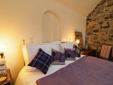 A bedroom with a bed with purple pillows and blanket beside a stone wall at The Croft in Newtown-Crommelin near Cloughmills