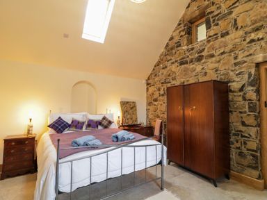 A bedroom with a metal bed frame a wooden wardrobe a stone wall and bedside tables at The Croft in Newtown-Crommelin near Cloughmills