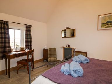 A bedroom with a bed holding blue towels a wooden desk with chair and a window with checkered curtains at The Croft in Newtown-Crommelin near Cloughmills