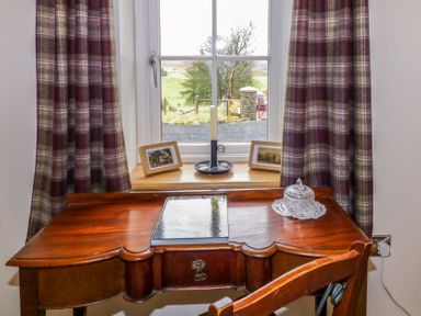 A wooden desk with a book and glass container in front of a window with plaid curtains at The Croft in Newtown-Crommelin near Cloughmills
