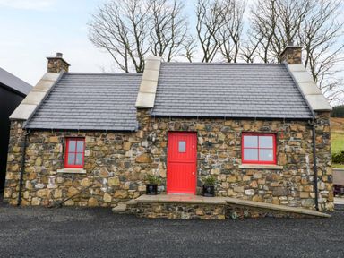 A stone cottage with a red door and two red windows with a gray roof at The Croft in Newtown-Crommelin near Cloughmills