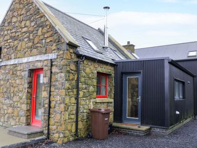 A stone house with a red door and window next to a black structure with a glass door at The Croft in Newtown-Crommelin near Cloughmills