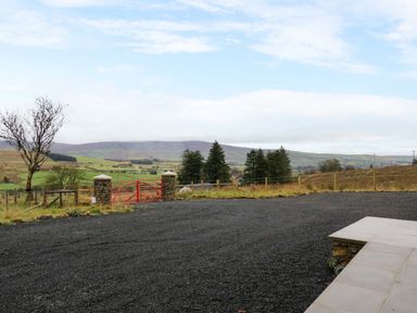 A gravel driveway with a red gate and stone pillars overlooking green fields and hills at The Croft in Newtown-Crommelin near Cloughmills