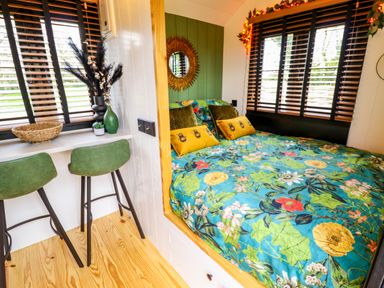 A bedroom with a floral bedspread green chairs and windows with wooden blinds at Herdwick Luxury Glamping in Nottingham