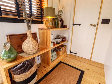 A corner with wooden shelves holding decor items and kitchenware next to a white door at Herdwick Luxury Glamping in Nottingham