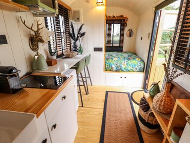 A small kitchen and sleeping area with a stove kettle and coffee machine and a bed with floral bedding at Herdwick Luxury Glamping in Nottingham