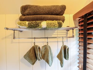 A chrome towel rack with folded towels on top and hanging washcloths beside a window with wooden blinds at Herdwick Luxury Glamping Nottingham