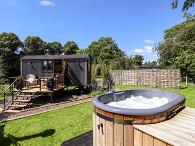 An outdoor area with a hot tub and a raised cabin with stairs and seating at Herdwick Luxury Glamping in Nottingham