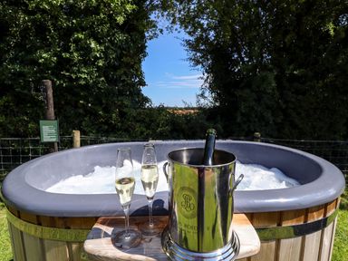 A hot tub with bubbling water outdoors next to a wooden platform holding two champagne glasses and a champagne bottle in an ice bucket at Herdwick Luxury Glamping in Nottingham