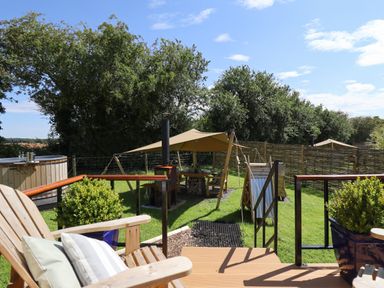 An outdoor seating area with wooden chairs and cushions near a hot tub and a sheltered dining area at Herdwick Luxury Glamping in Nottingham