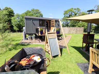 An outdoor setup with a cast iron pan cooking breakfast in front of a grey corrugated cabin at Herdwick Luxury Glamping in Nottingham