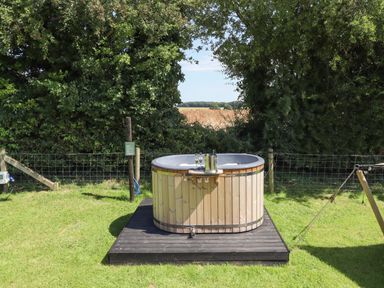An outdoor hot tub on a wooden platform with champagne glasses and an ice bucket on the edge in a grassy area surrounded by trees at Herdwick Luxury Glamping in Nottingham