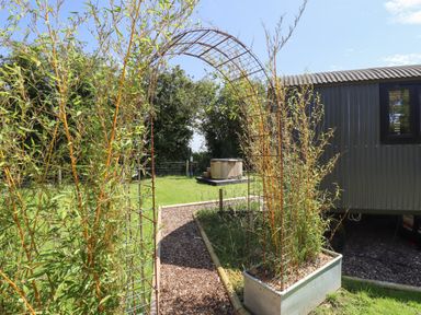 A garden path with a metal arch trellis and plants leading to a hot tub and a dark exterior building at Herdwick Luxury Glamping in Nottingham