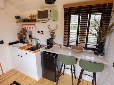 A kitchen area with a sink stove microwave coffee machine small fridge and two green chairs at Southdown Luxury Glamping in Nottingham