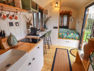 A compact kitchen and dining area with a sink kettle coffee machine stools and a bed with floral bedding at Southdown Luxury Glamping in Nottingham