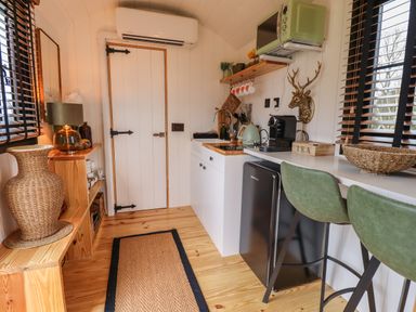 A small kitchen with green stools black mini fridge and wooden shelves with a woven basket at Southdown Luxury Glamping in Nottingham