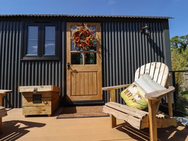 A wooden chair with cushions and a boot box outside a door with a wreath on a corrugated metal building at Southdown Luxury Glamping in Nottingham
