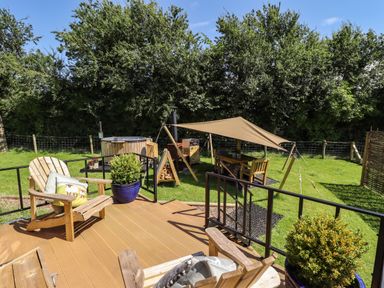 A wooden deck with chairs and cushions overlooking a garden area with a table under a canopy and a hot tub at Southdown Luxury Glamping in Nottingham