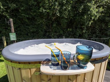 An outdoor hot tub with bubbles with two blue glasses and a blue pitcher on a small wooden table at Southdown Luxury Glamping in Nottingham