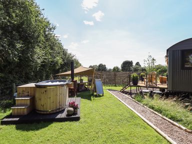 An outdoor area with a wooden hot tub a canopy tent with a table and chairs and a raised deck with wooden chairs at Southdown Luxury Glamping in Nottingham