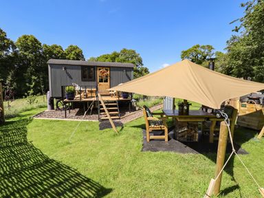 A small corrugated metal cabin with a wooden door and deck next to a shaded outdoor seating area with wooden furniture at Southdown Luxury Glamping in Nottingham