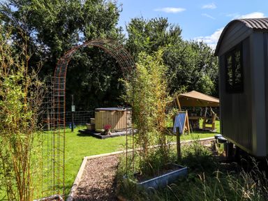 A garden area with a metal archway wooden hot tub tent and outdoor seating at Southdown Luxury Glamping in Nottingham