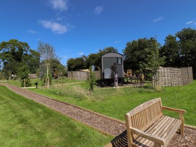 An outdoor area with wooden benches on a path and small cabins surrounded by trees and fences at Southdown Luxury Glamping in Nottingham