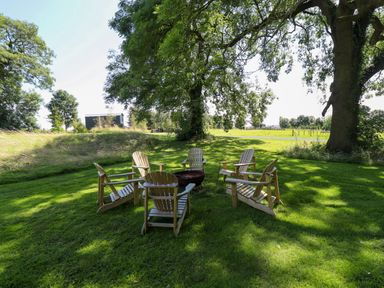 Six wooden chairs arranged in a circle around a fire pit on a grass lawn under large trees at Southdown Luxury Glamping in Nottingham