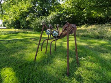 A metal sculpture of an insect on grass with trees in the background at Southdown Luxury Glamping in Nottingham