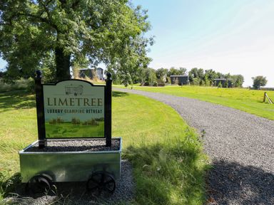A gravel pathway leading to small buildings in a grassy field with a sign for Limetree Luxury Glamping Retreat