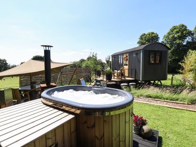 An outdoor area with a wooden hot tub and a small black cabin on wheels at Southdown Luxury Glamping in Nottingham