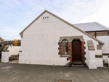 A white building with a wooden door and a small window at East Point Lynas Lighthouse Keeper's Cottage in Llaneilian near Amlwch