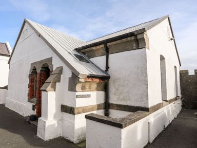 A white cottage with a slanted roof and stone trim near a paved area at East Point Lynas Lighthouse Keeper's Cottage Llaneilian near Amlwch