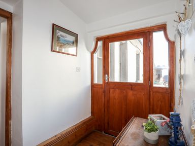 An entryway with a wooden door and window panels a small wooden table with a plant and lantern on it and a framed picture on the wall at East Point Lynas Lighthouse Keeper's Cottage in Llaneilian near Amlwch