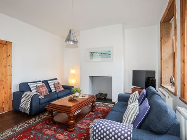 A living room with two blue sofas and a wooden coffee table on a red patterned rug at East Point Lynas Lighthouse Keeper's Cottage in Llaneilian near Amlwch
