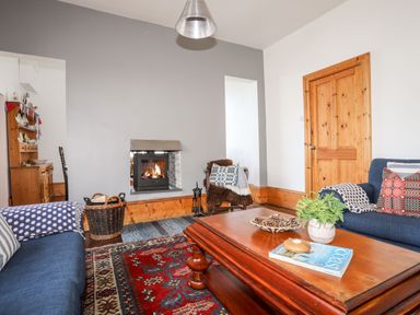 A living room with a fireplace wooden coffee table blue sofas patterned cushions and a rug at East Point Lynas Lighthouse Keeper's Cottage Llaneilian near Amlwch