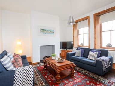 A living room with two blue sofas a wooden coffee table a patterned red rug and a television at East Point Lynas Lighthouse Keeper's Cottage in Llaneilian near Amlwch
