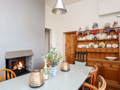 A dining room with a table set with flowers and candles next to a fireplace and a wooden cabinet with plates at East Point Lynas Lighthouse Keeper's Cottage in Llaneilian near Amlwch