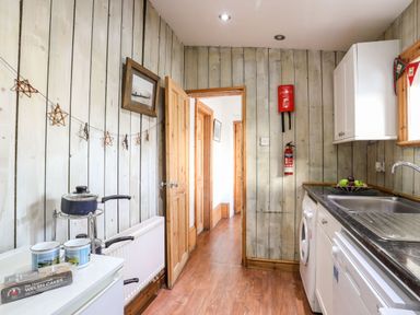 A kitchen with wooden walls a pot on a stand a washing machine and a sink at East Point Lynas Lighthouse Keeper's Cottage in Llaneilian near Amlwch