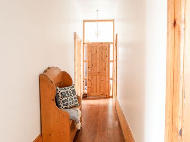 A hallway with wooden flooring a wooden bench with a patterned cushion and blanket and a wooden door at East Point Lynas Lighthouse Keeper's Cottage in Llaneilian near Amlwch