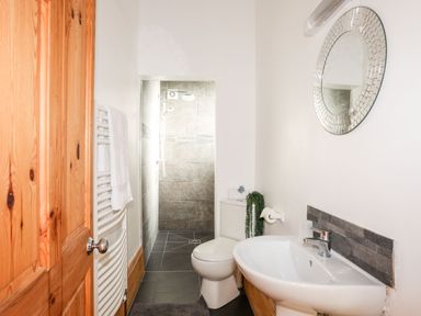 A bathroom with a wooden door a white sink a toilet a round mirror and a shower at East Point Lynas Lighthouse Keeper's Cottage in Llaneilian near Amlwch