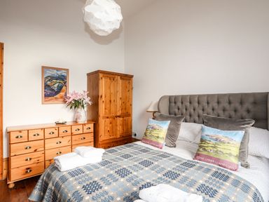 A bedroom with a bed with pillows and a blanket two wooden cupboards a painting and a vase with flowers at East Point Lynas Lighthouse Keeper's Cottage Llaneilian near Amlwch