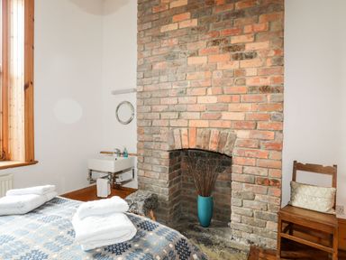 A bedroom corner with a brick fireplace a wooden chair a small sink and towels on a bed at East Point Lynas Lighthouse Keeper's Cottage in Llaneilian near Amlwch