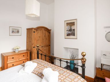 A bedroom with a wooden wardrobe and chest of drawers a metal bed frame and a white sink at East Point Lynas Lighthouse Keeper's Cottage Llaneilian near Amlwch