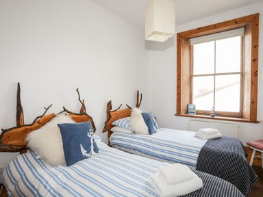 A bedroom with two single beds with striped bedding and wooden headboards beside a window at East Point Lynas Lighthouse Keeper's Cottage in Llaneilian near Amlwch