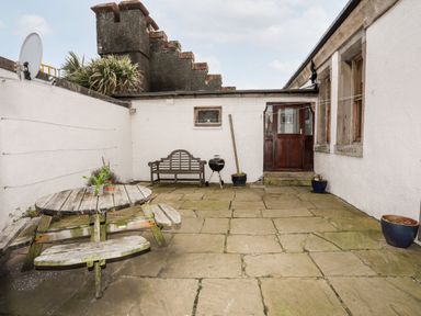 A stone patio with wooden picnic table bench seating wooden bench charcoal grill and potted plants at East Point Lynas Lighthouse Keeper's Cottage in Llaneilian near Amlwch