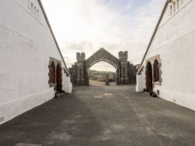 A paved courtyard between two white buildings with an arched stone gate at East Point Lynas Lighthouse Keeper's Cottage in Llaneilian near Amlwch
