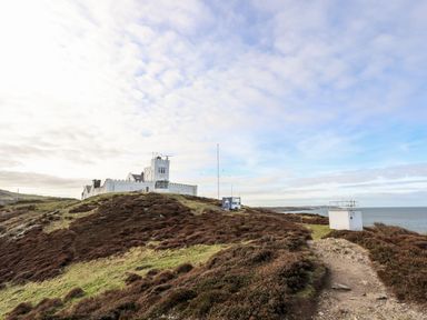 A coastal landscape with a white building and path overlooking the sea at East Point Lynas Lighthouse Keeper's Cottage in Llaneilian near Amlwch