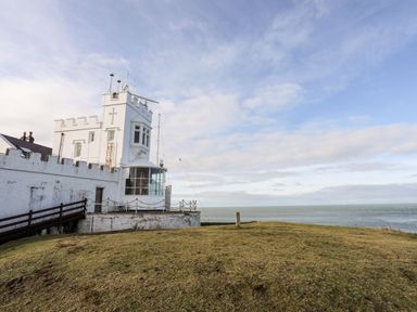 A white lighthouse with a fenced balcony on a grassy hill by the sea at East Point Lynas Lighthouse Keeper's Cottage in Llaneilian near Amlwch